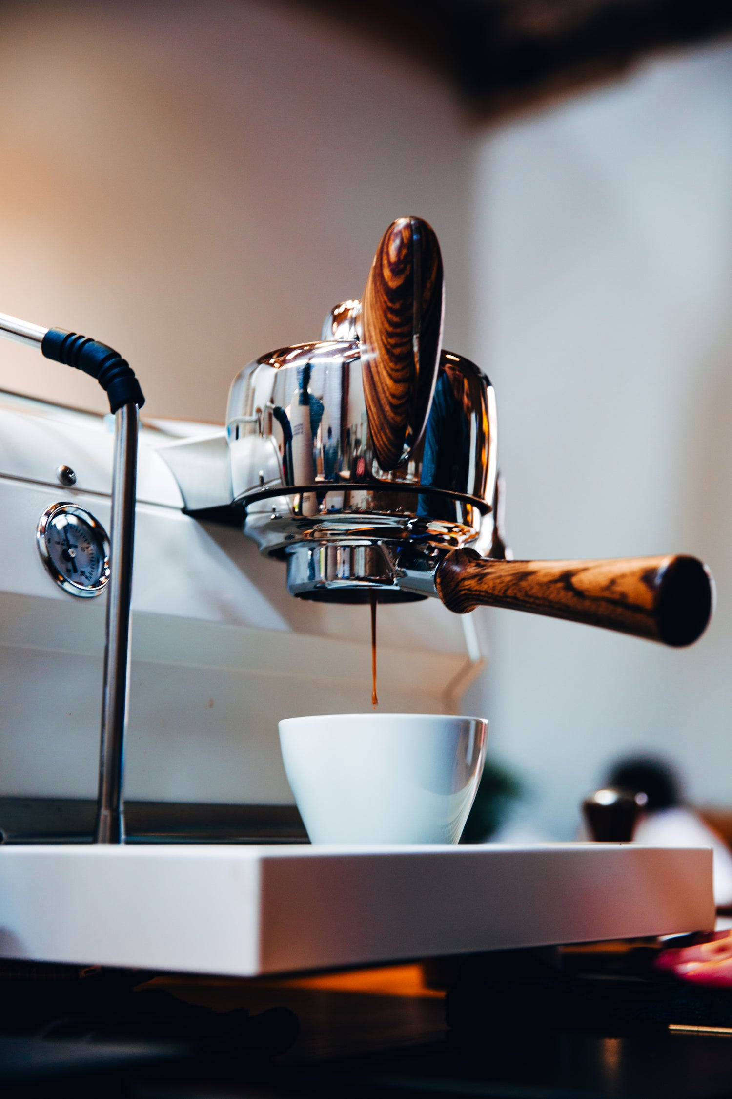 Close-up of a wood-handled espresso machine pouring fresh coffee into a white cup, highlighting rich crema and artisanal brewing.